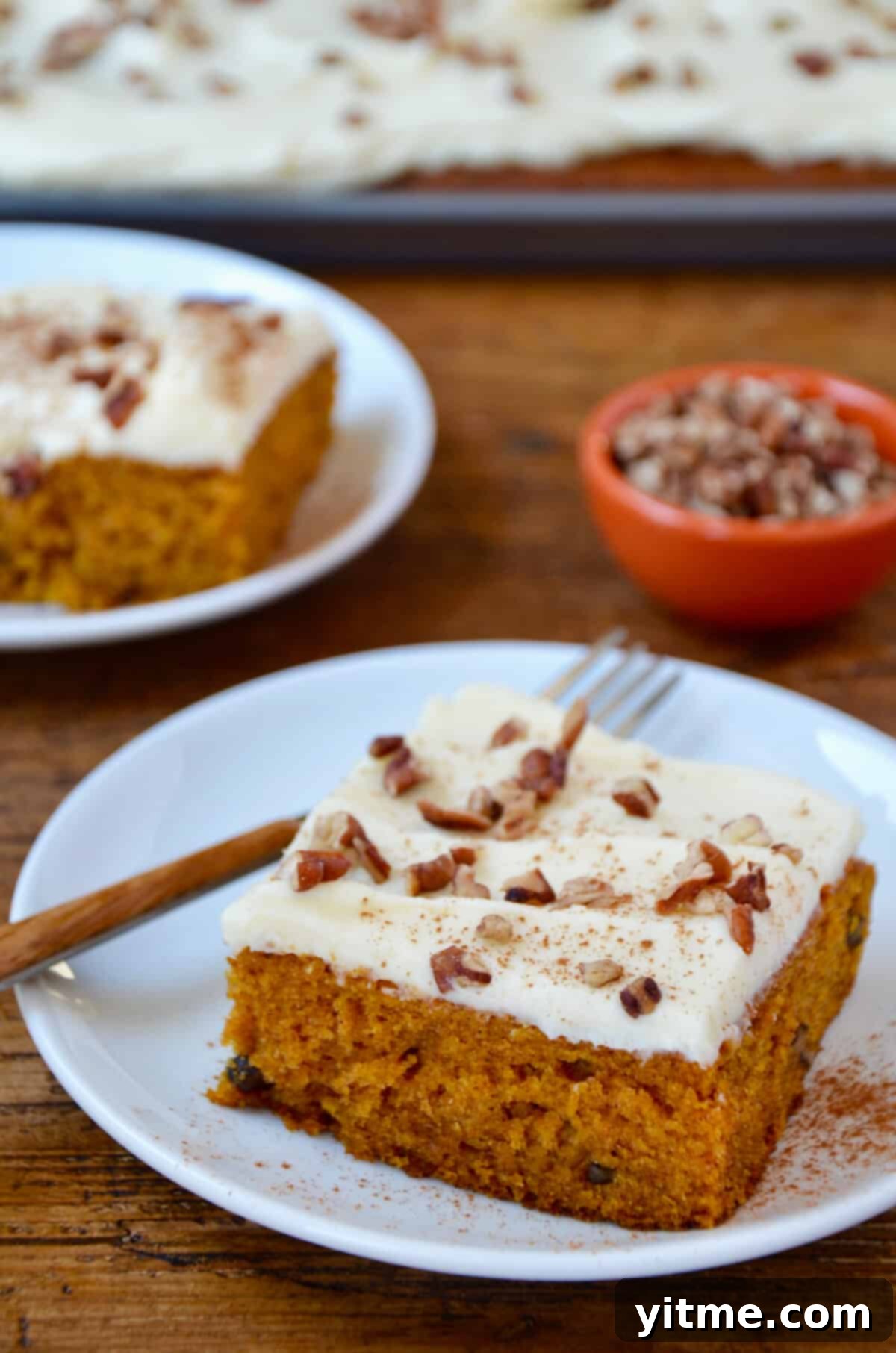 Slices of pumpkin bars with cream cheese frosting and pecans on white plates.