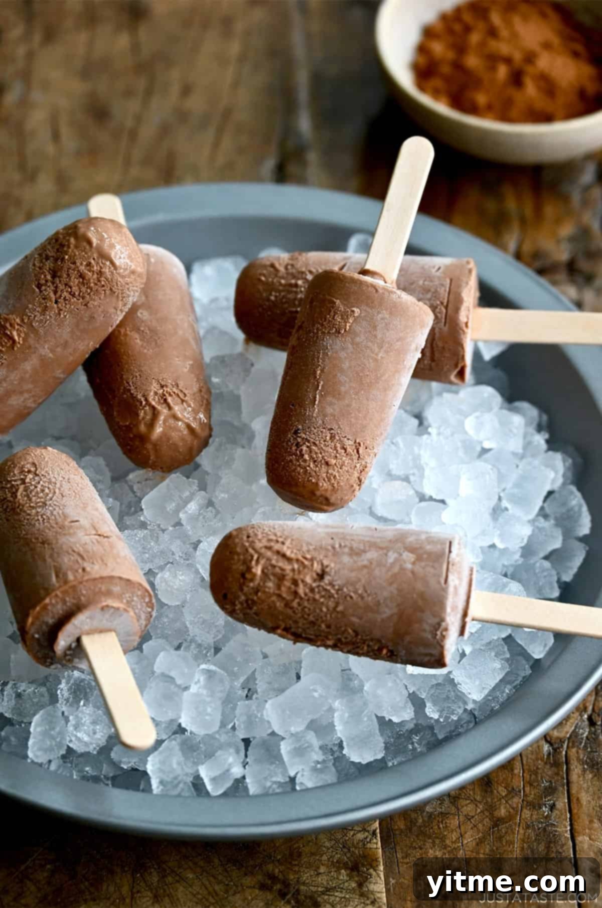 Several homemade fudge pops with wooden sticks, resting on a bed of ice, ready to be enjoyed as a refreshing summer dessert.