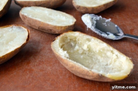 A baked potato with its interior scooped out and a spoon sitting beside it. More baked potatoes are off to the side.