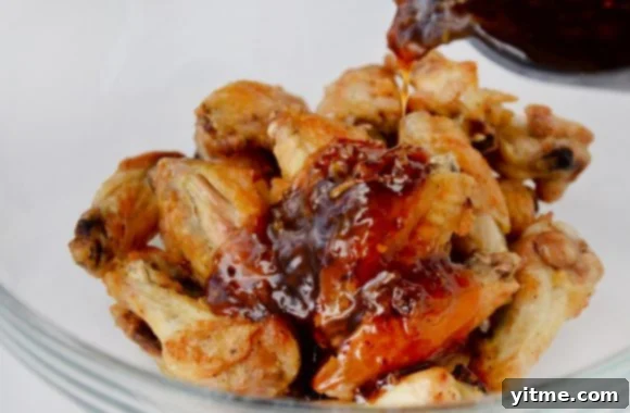 Zesty Orange Baked Chicken Wings 5 Baked chicken wings in a glass bowl with orange sauce being poured over them.