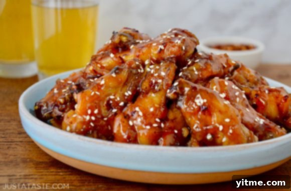 Zesty Orange Baked Chicken Wings 6 Crispy Baked Orange Chicken Wings on a pale blue plate garnished with sesame seeds; two glasses of beer and a small ramekin with red pepper flakes in the background.