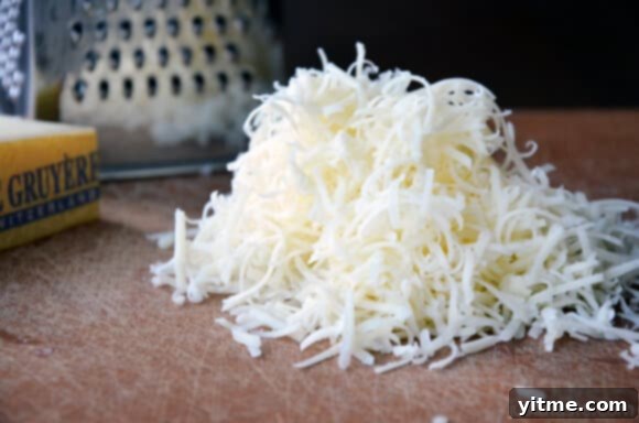 A pile of freshly shredded Gruyere cheese, highlighting its rich texture and color.