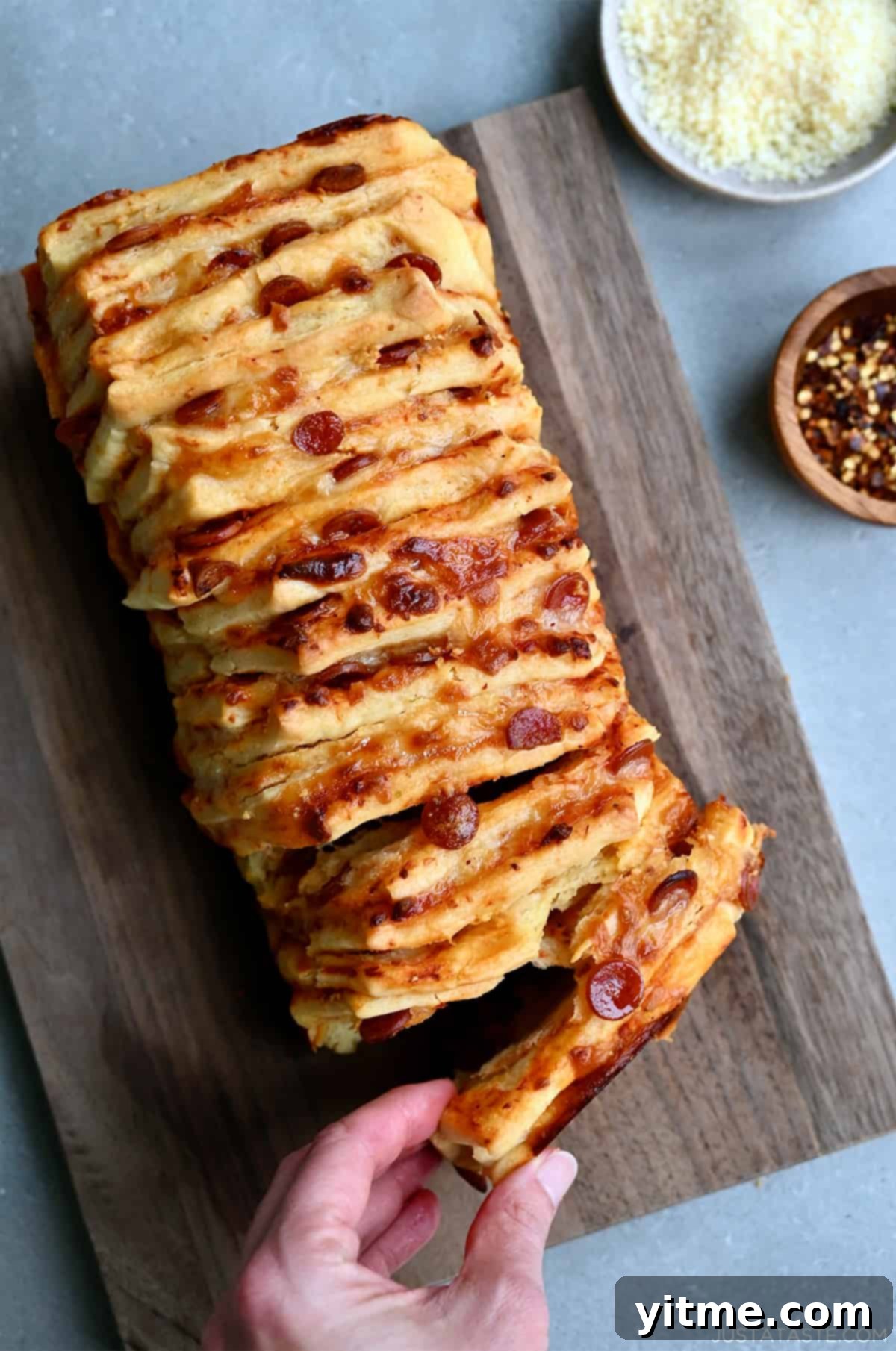 A hand reaches for a pepperoni pull-apart pizza bread on a wood cutting board. 