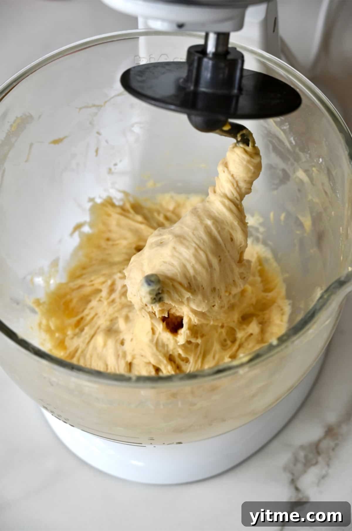 A stand mixer with the dough hook covered with pizza dough.