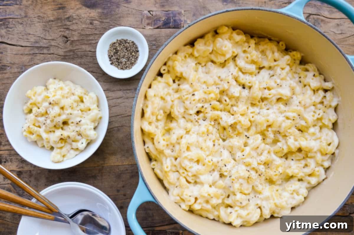 A blue Dutch oven filled with white cheddar mac and cheese sits on a wooden surface.