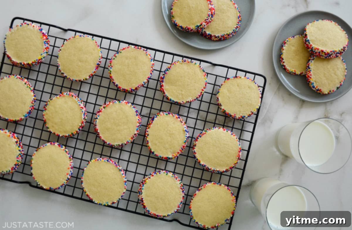 Slice-and-Bake Butter Cookies studded with rainbow sprinkles on a wire cooling rack next to two glasses of milk.