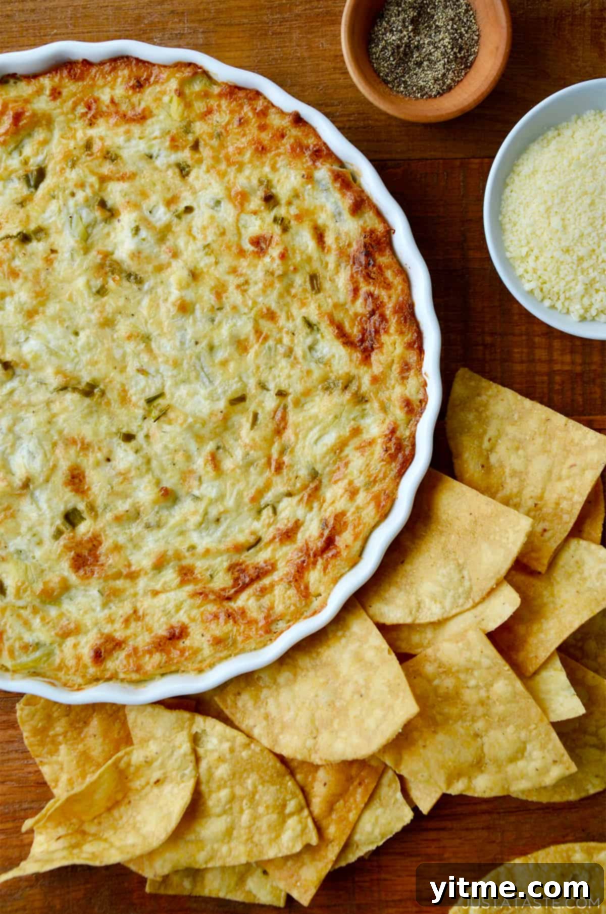 A white baking dish containing warm artichoke dip surrounded by tortilla chips.
