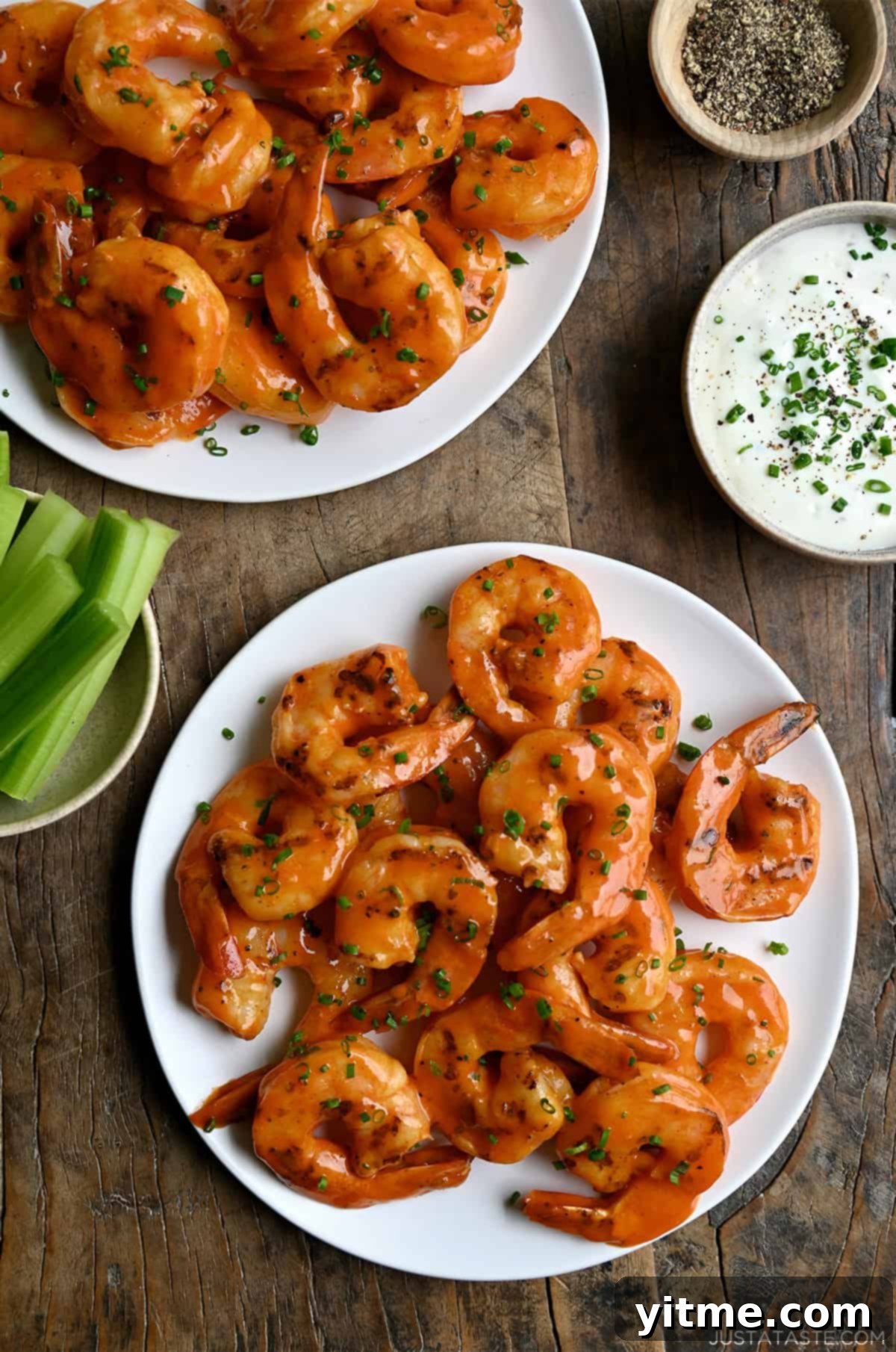 Grilled buffalo shrimp on a white plate next to a bowl with celery sticks and a bowl with ranch dressing.