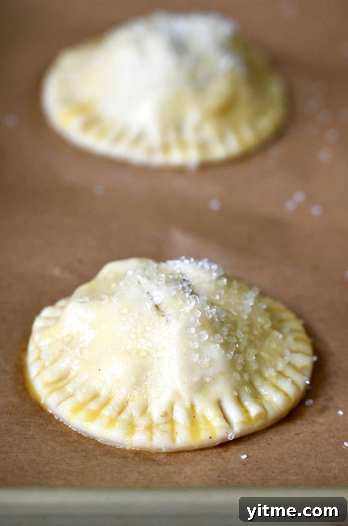 Unbaked hand pies generously topped with sparkling sanding sugar, ready to be baked to a beautiful golden finish.