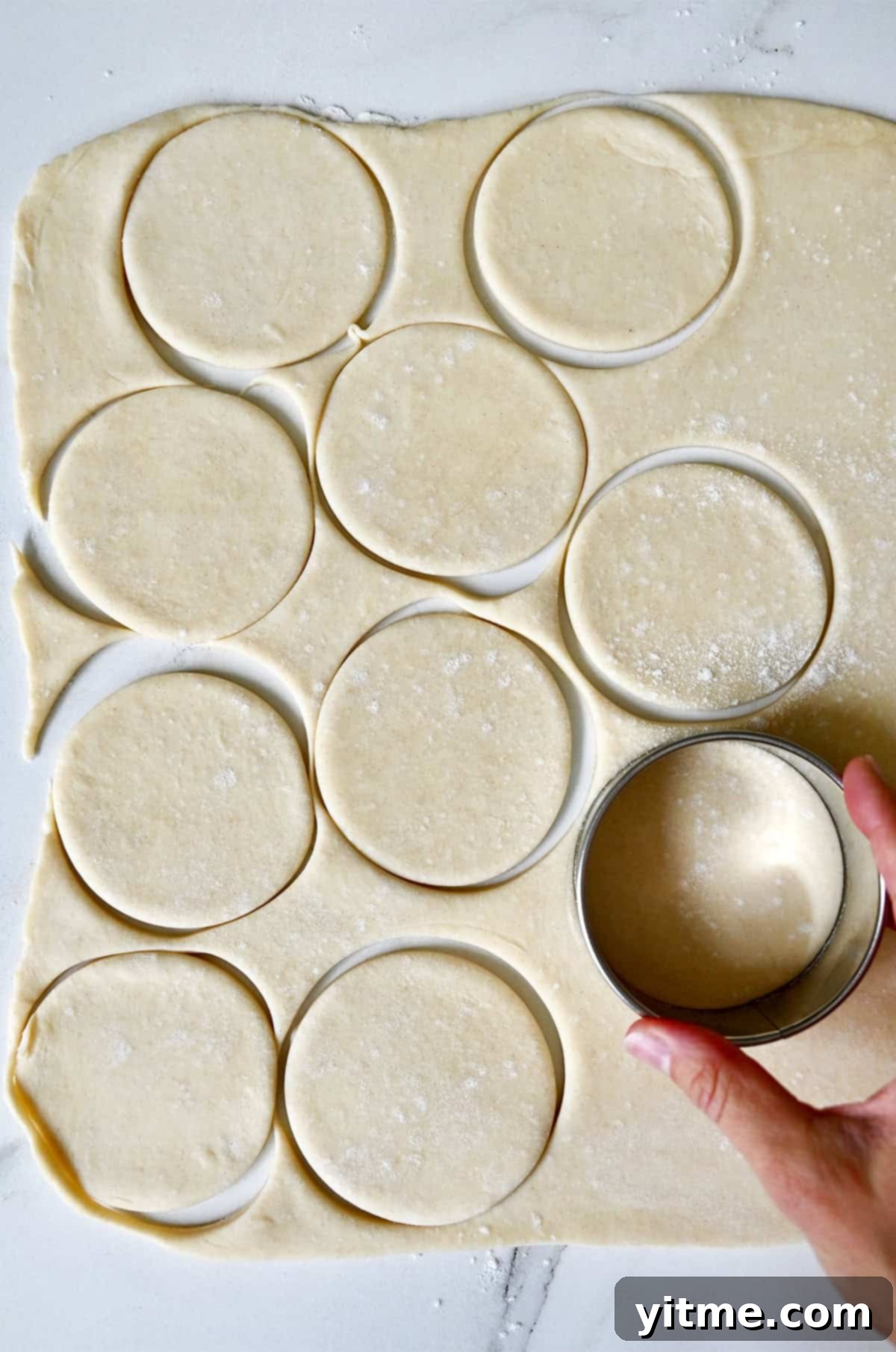 A hand pressing a circular cookie cutter into rolled-out pie dough to create individual pie bases, ensuring uniform shapes.