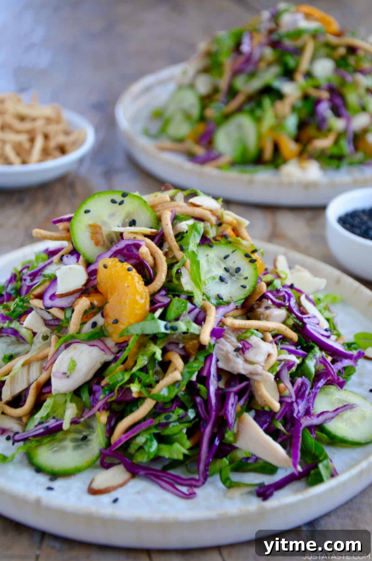 Chinese chicken salad with cucumbers, mandarin oranges, crispy chow mein noodles, shredded purple cabbage and romaine lettuce all tossed in a sesame dressing and garnished with black sesame seeds.