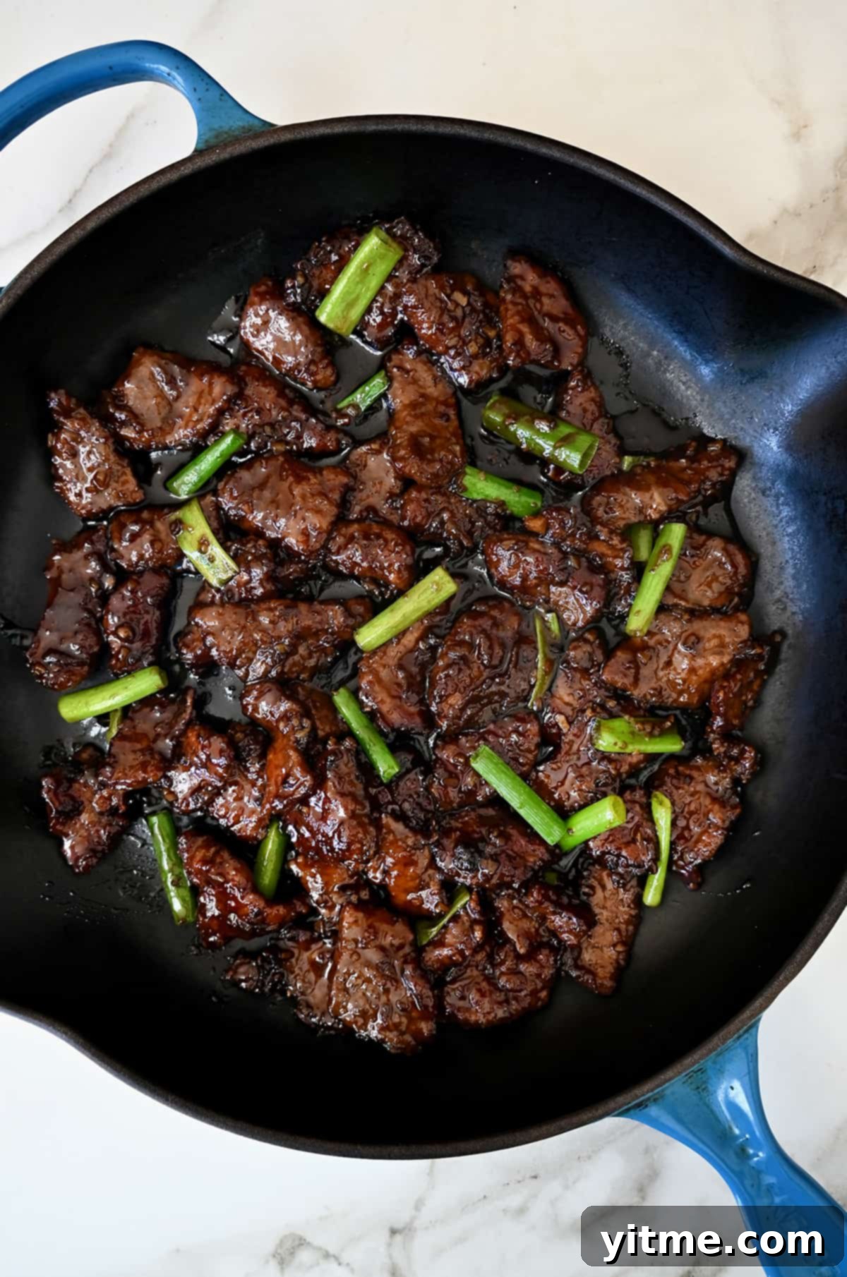 A large skillet containing Mongolian beef with sliced scallions.