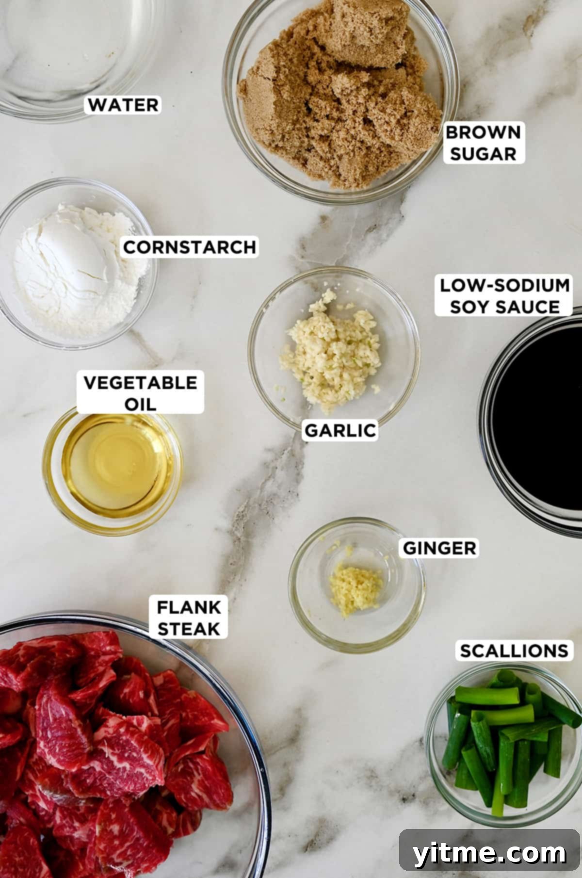 Various sizes of clear bowls containing ingredients to make Mongolian beef, including brown sugar, low-sodium soy sauce, scallions, minced ginger, minced garlic, thinly sliced flank steak, vegetable oil and cornstarch.