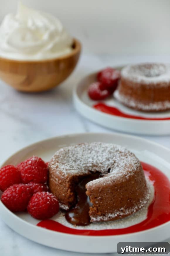 Chocolate Lava Cakes with Raspberry Sauce on dessert plates with fresh raspberries; bowl with whipped cream