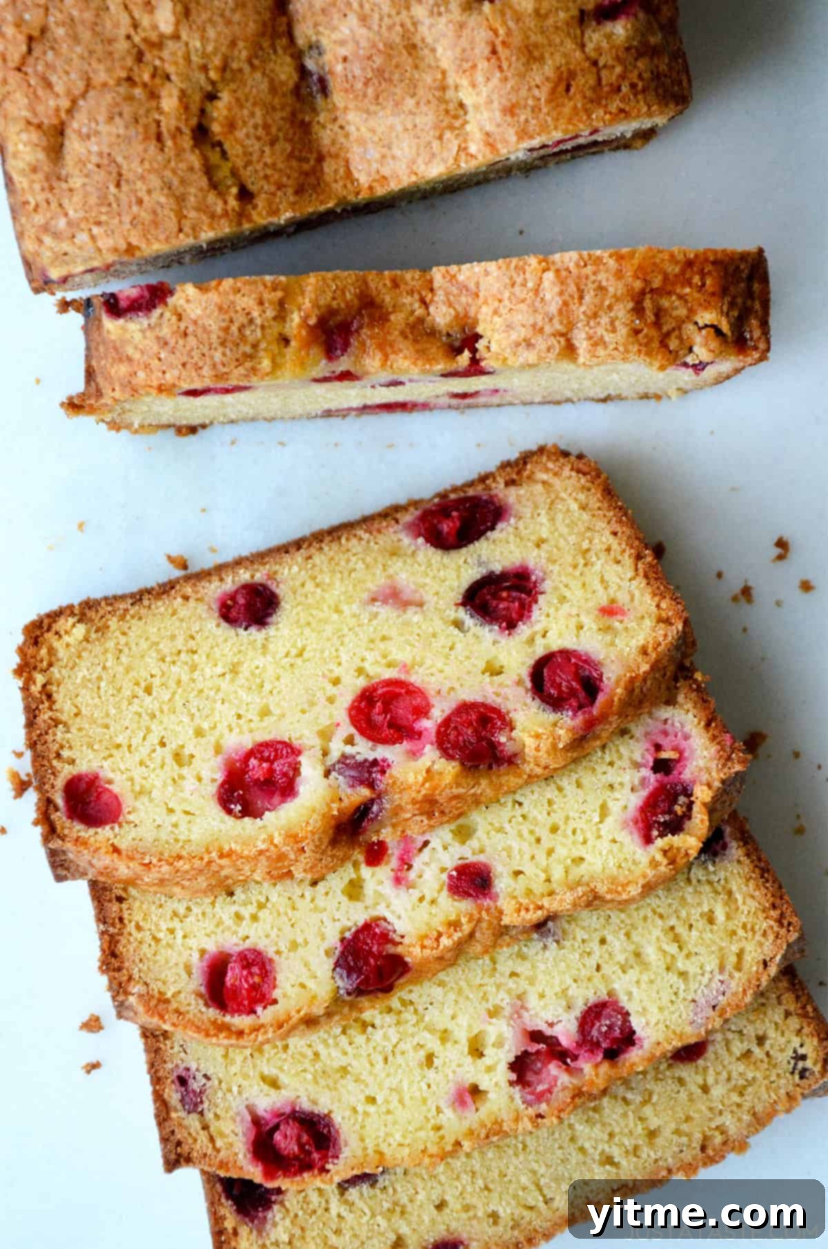 A loaf of cranberry orange bread cut into slices, showcasing the juicy cranberries and moist crumb.