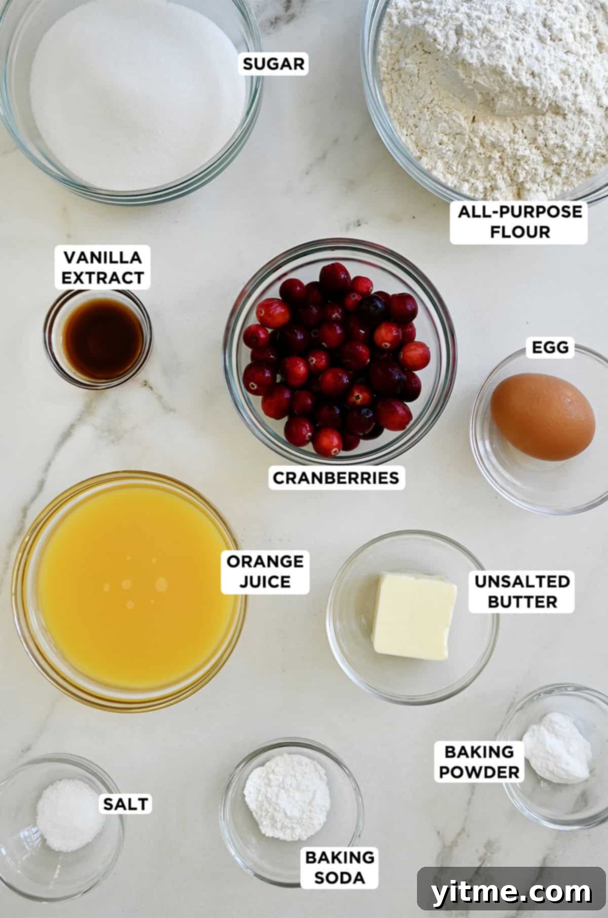 Orange cranberry bread ingredients displayed in various sizes of clear glass bowls.