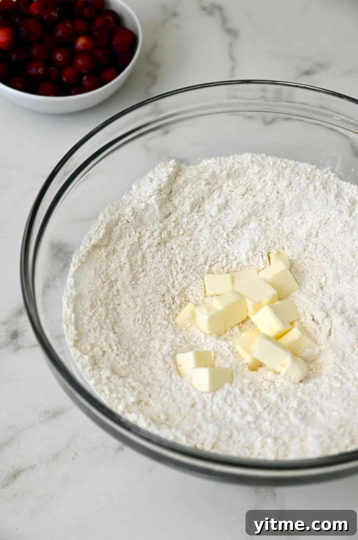 Cold, cubed butter resting atop flour in a glass bowl, ready to be cut in.