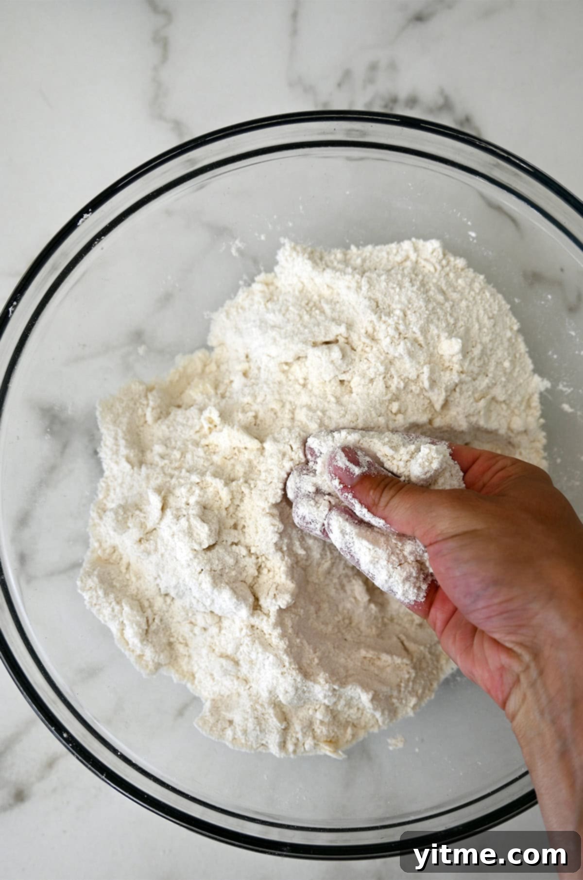 Hands demonstrating how to cut cold butter into flour mixture using fingertips.