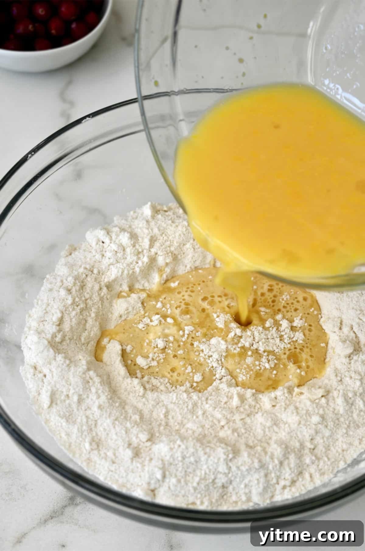 Orange juice being poured into a bowl containing flour mixture.