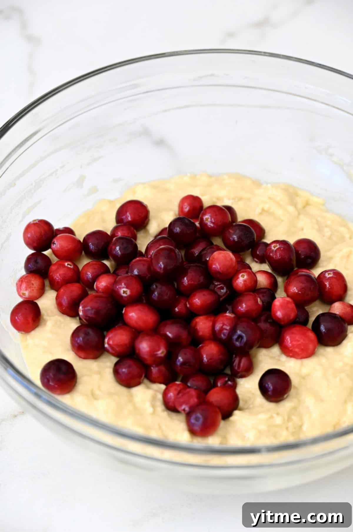 Fresh cranberries being gently folded into a bowl of quick bread batter.