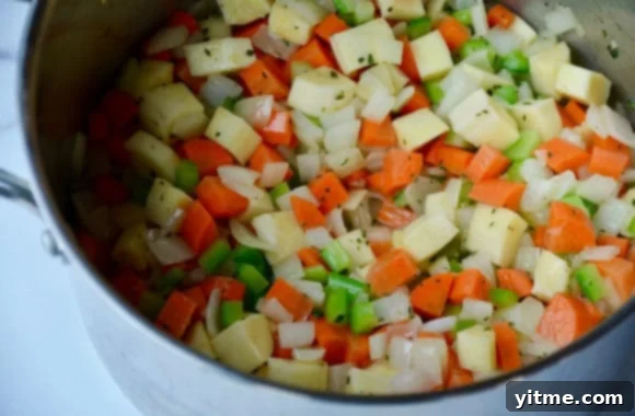 A large stockpot brimming with finely chopped root vegetables like onions, carrots, celery, and parsnips, along with fresh thyme, ready for the pot pie filling.