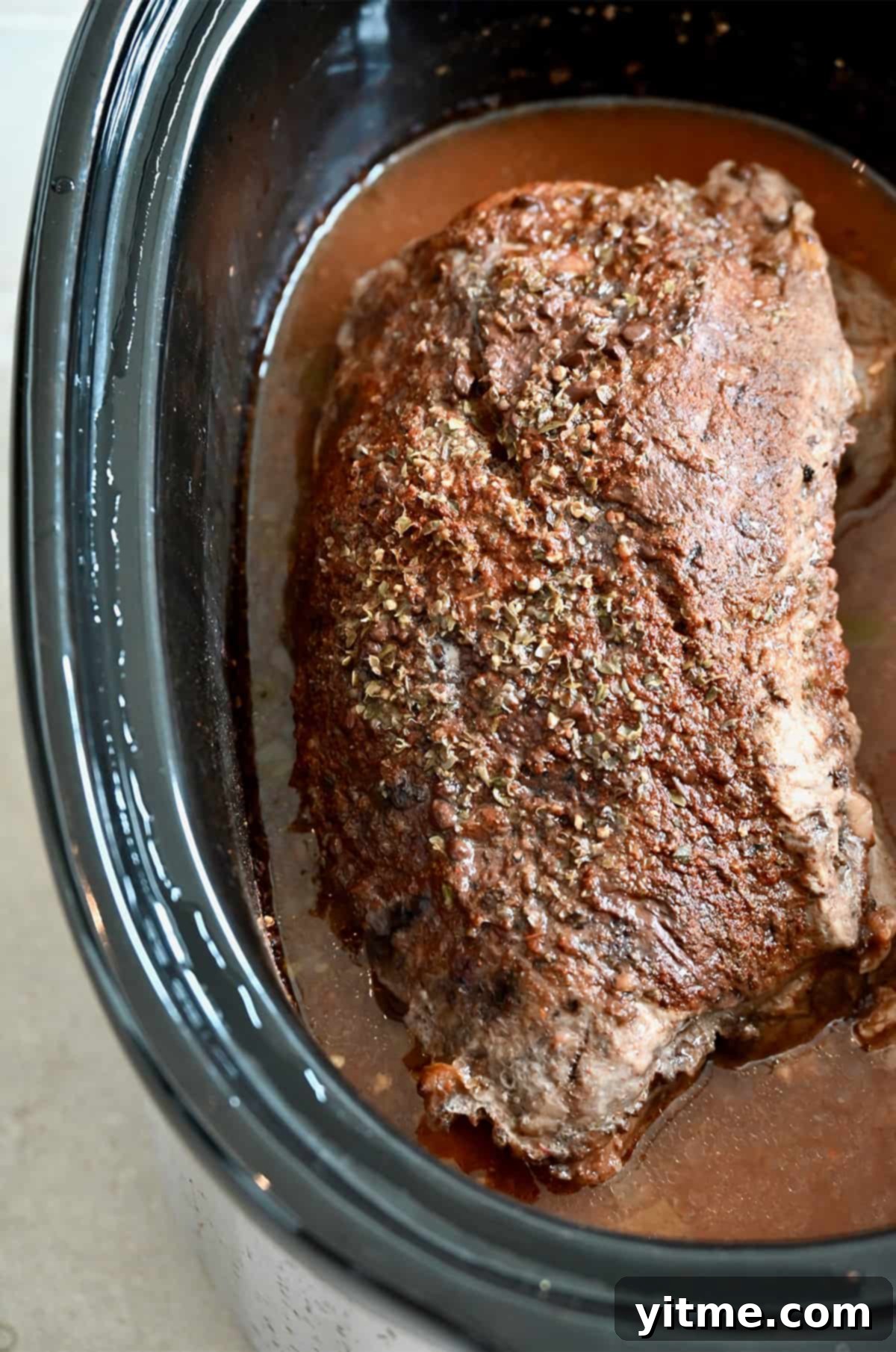 A whole, cooked pork roast in the bowl of a slow cooker.