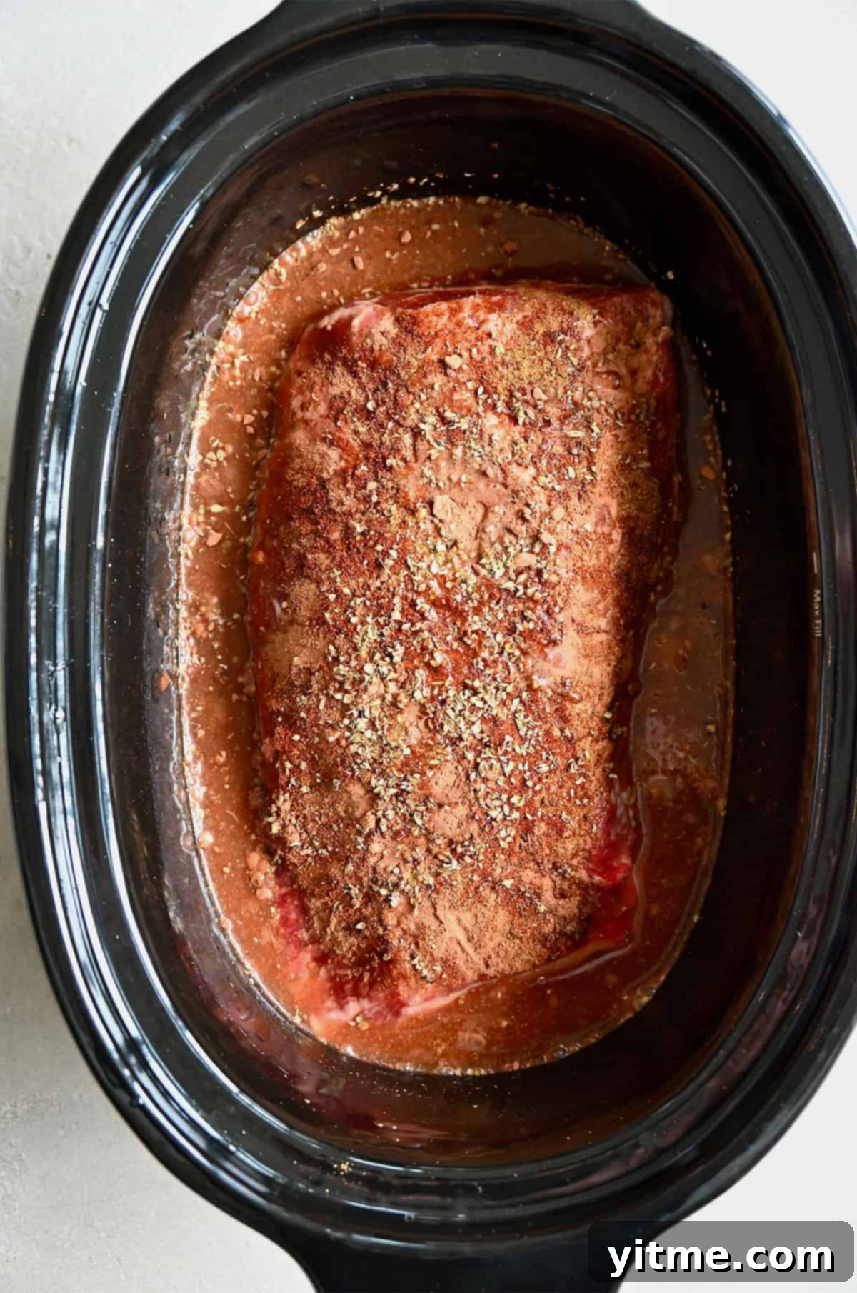 An uncooked pork roast seasoned with spices in the bowl of a slow cooker.