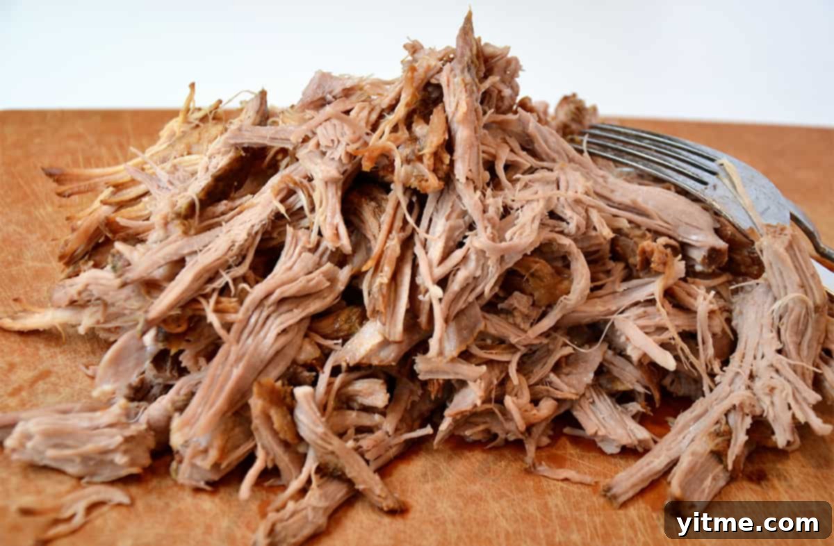 A pile of pulled pork on a cutting board. A fork sits beside the pork.