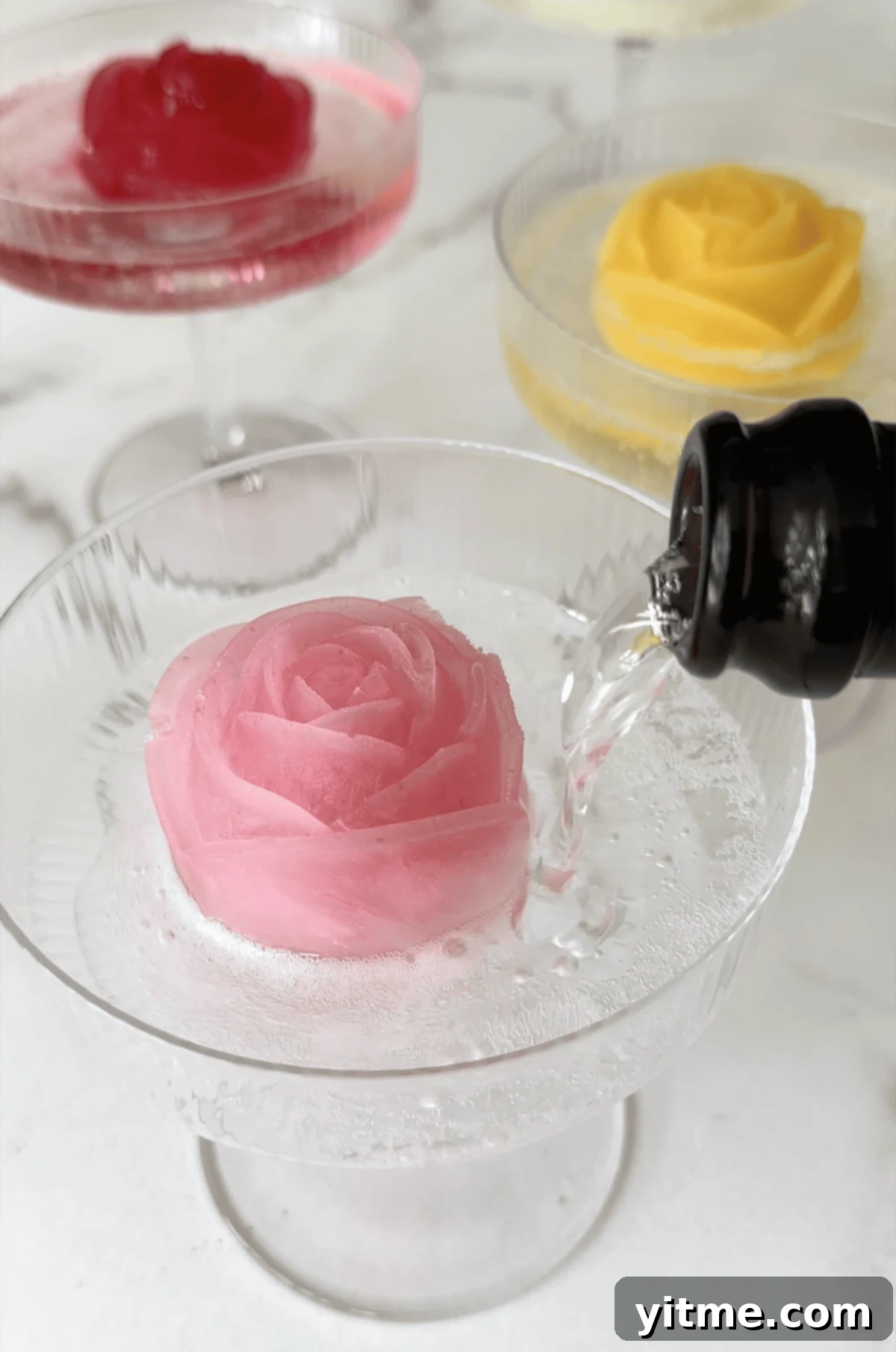 Champagne being poured over a lemonade ice cube in the shape of a rose in a cocktail glass.
