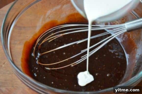 Milk being poured into chocolate molasses cake batter