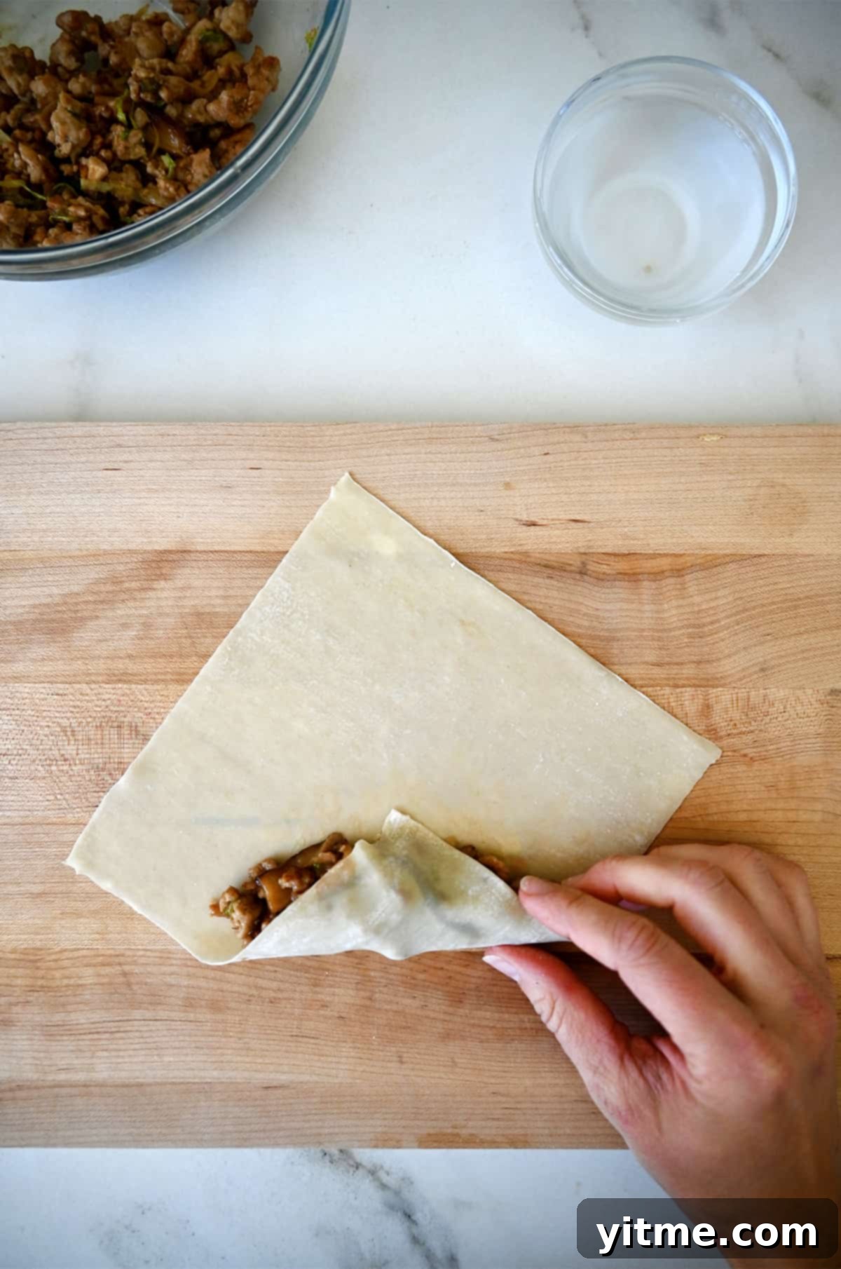 Folding the bottom edge of the wrapper over the filling.