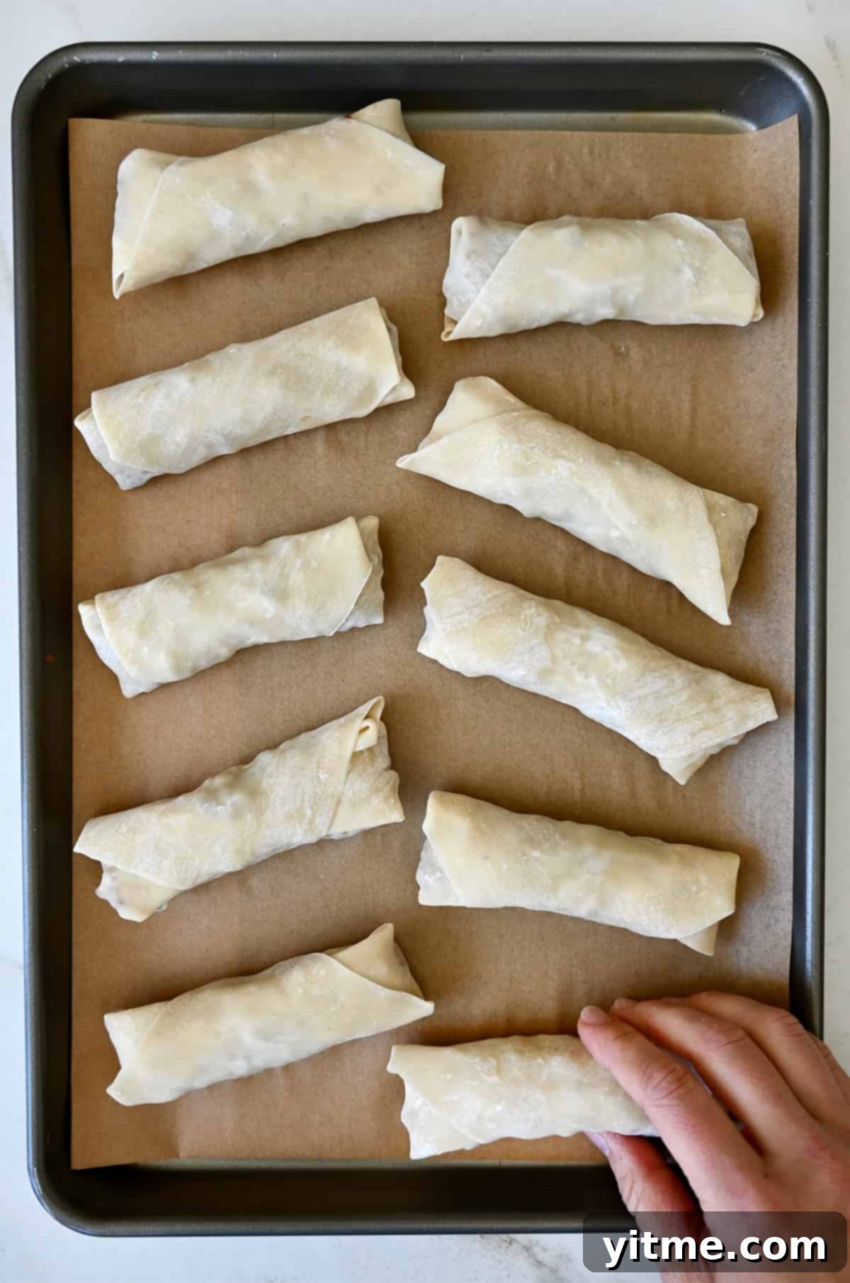 Unbaked chicken spring rolls on a baking sheet.
