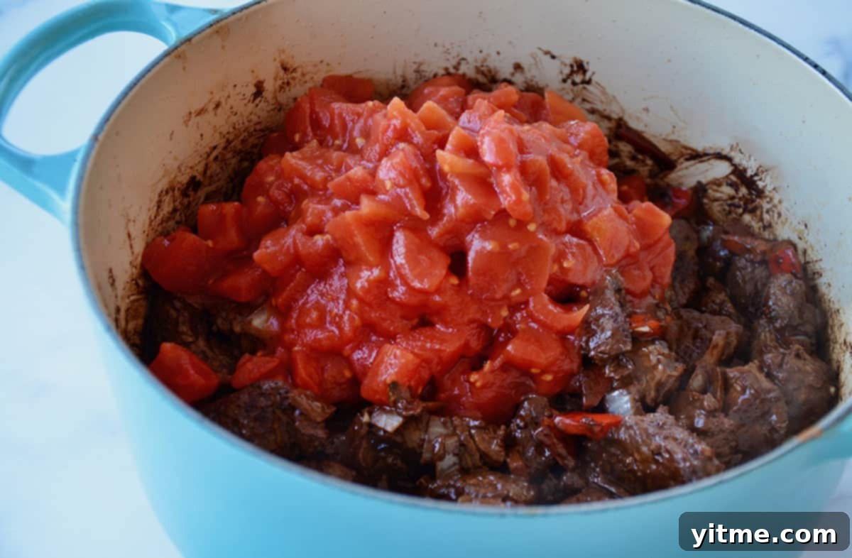 Chopped tomatoes added to the beef and vegetables in a Dutch oven