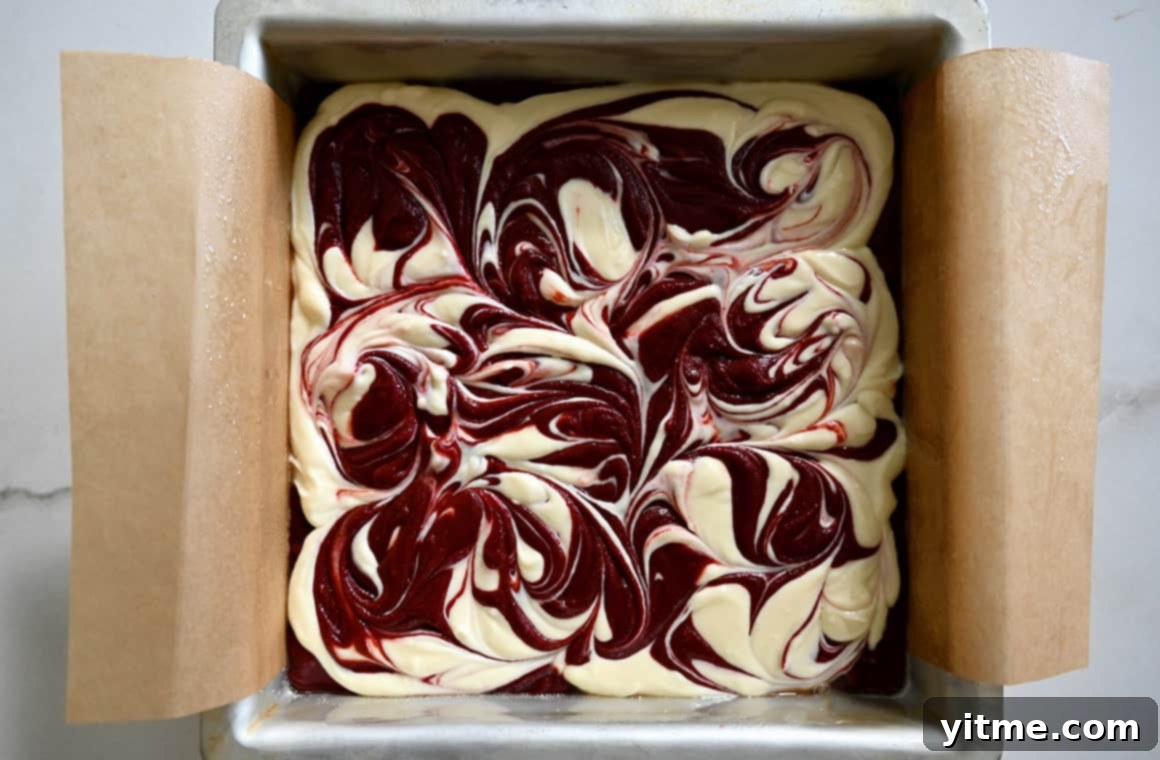 Swirled cheesecake brownie batter in a parchment paper-lined baking pan