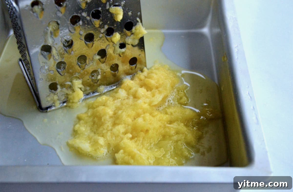 Fresh pineapple being grated with a box grater into a metal baking dish