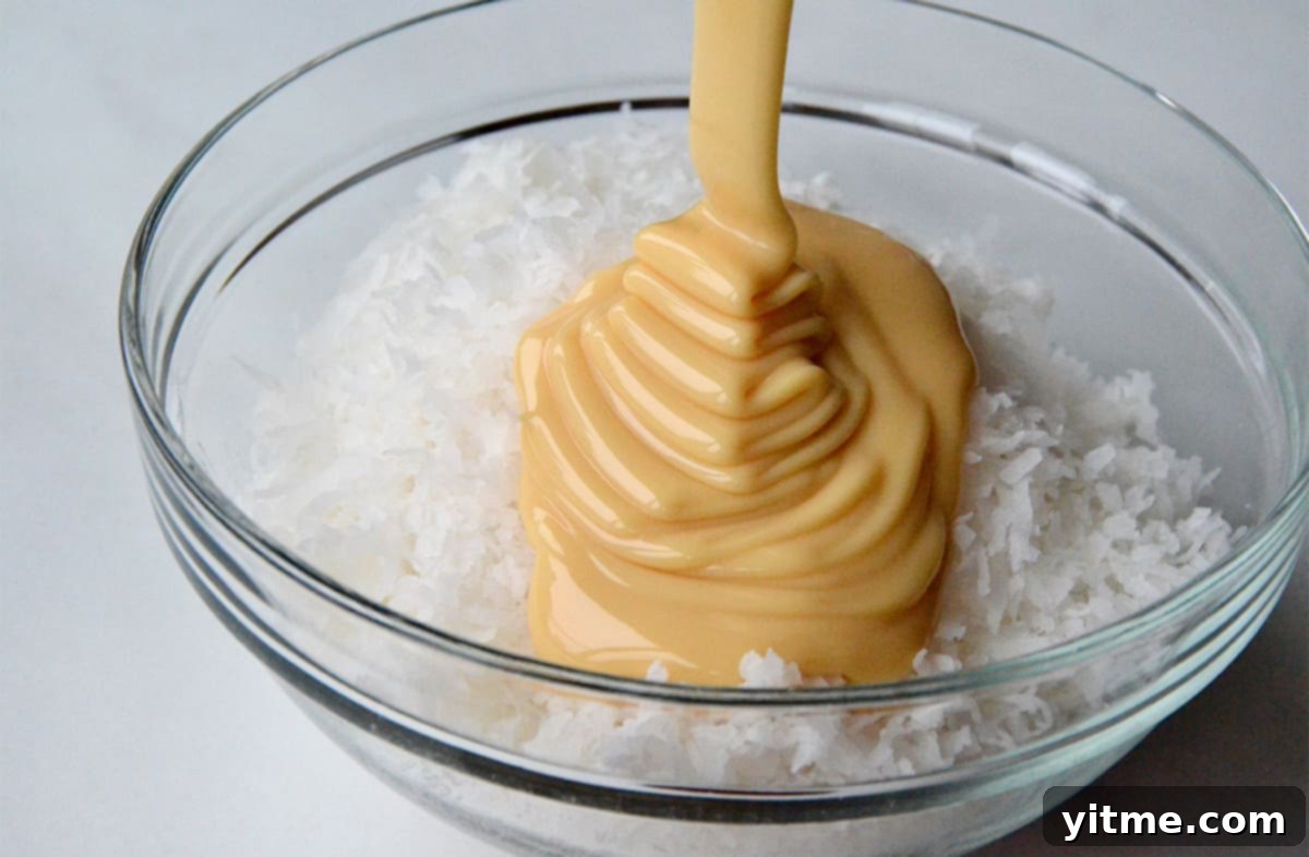 Sweetened condensed milk being drizzled over coconut in a glass bowl