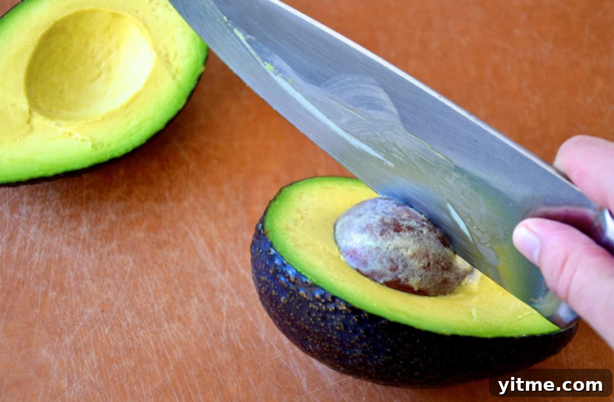 A person using a chef's knife to remove a pit from an avocado half.