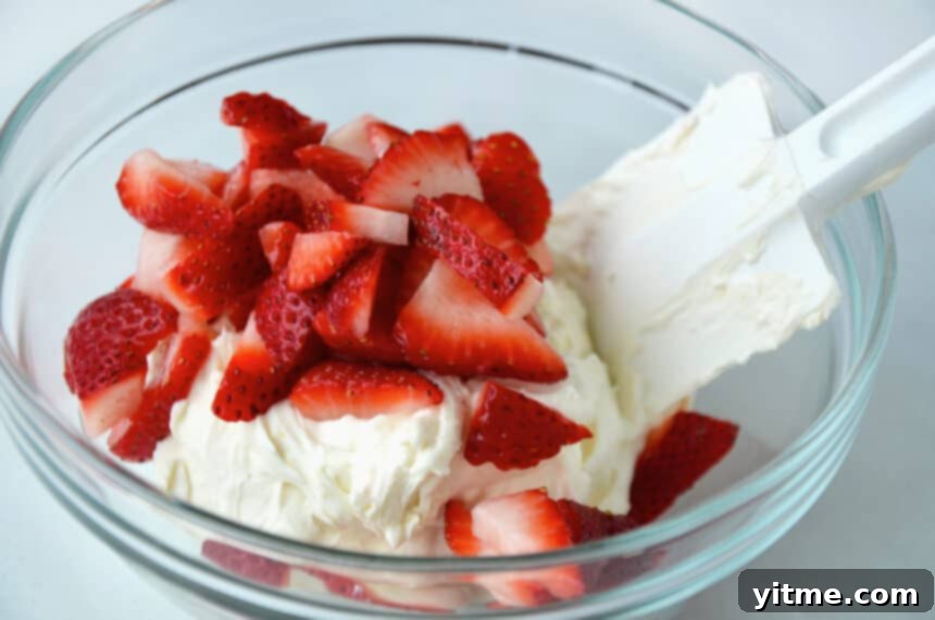 Spatula mixing cream cheese and fresh strawberries together in a clear bowl