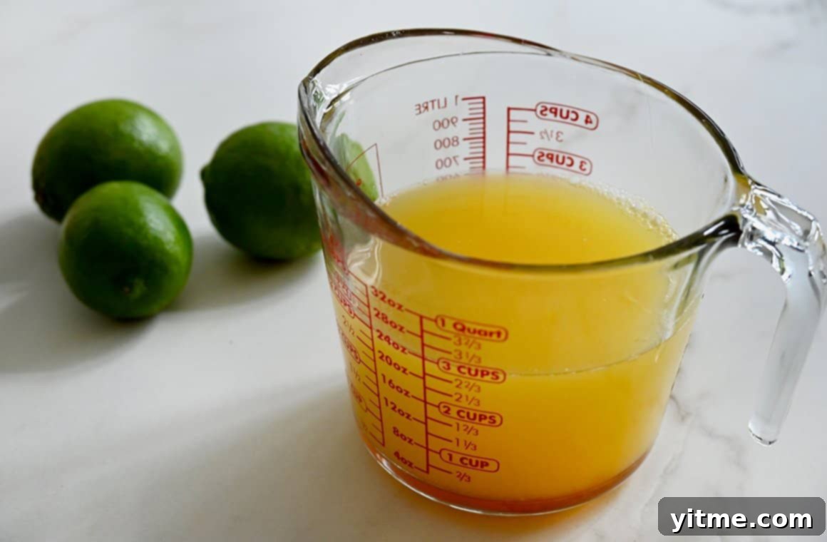 Boozy popsicle mixture in a glass measuring cup next to limes