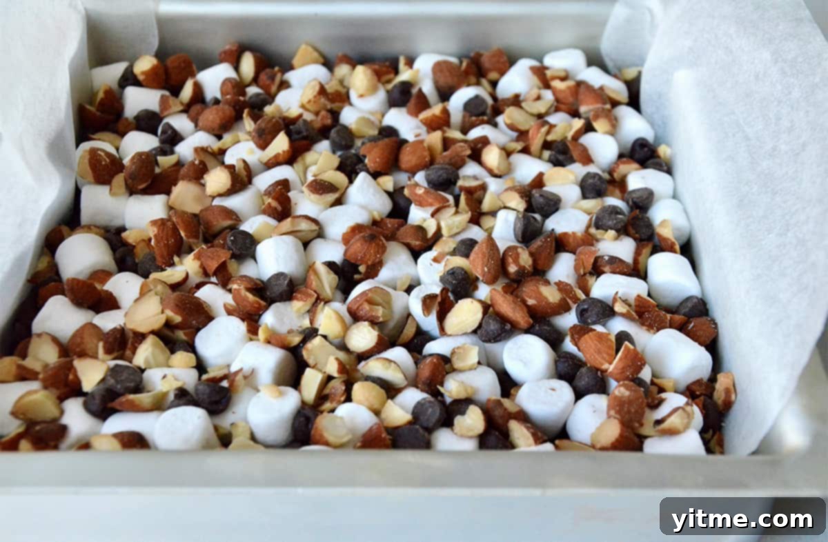 Rock road brownies in a square baking pan topped with chopped almonds, mini marshmallows and chocolate chips.