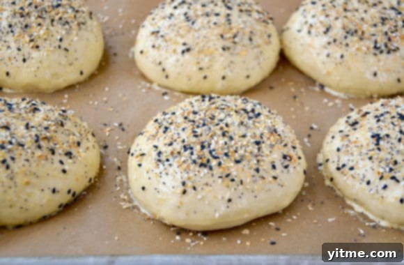 Unbaked burger buns neatly arranged on a baking sheet