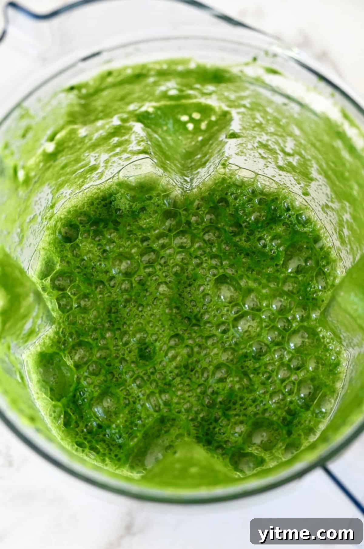 A blender jar is filled with green juice.