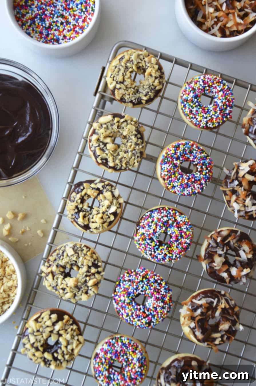 Baked Mini Buttermilk Doughnuts atop a wire cooling rack next to bowls containing Nutella Glaze and sprinkles