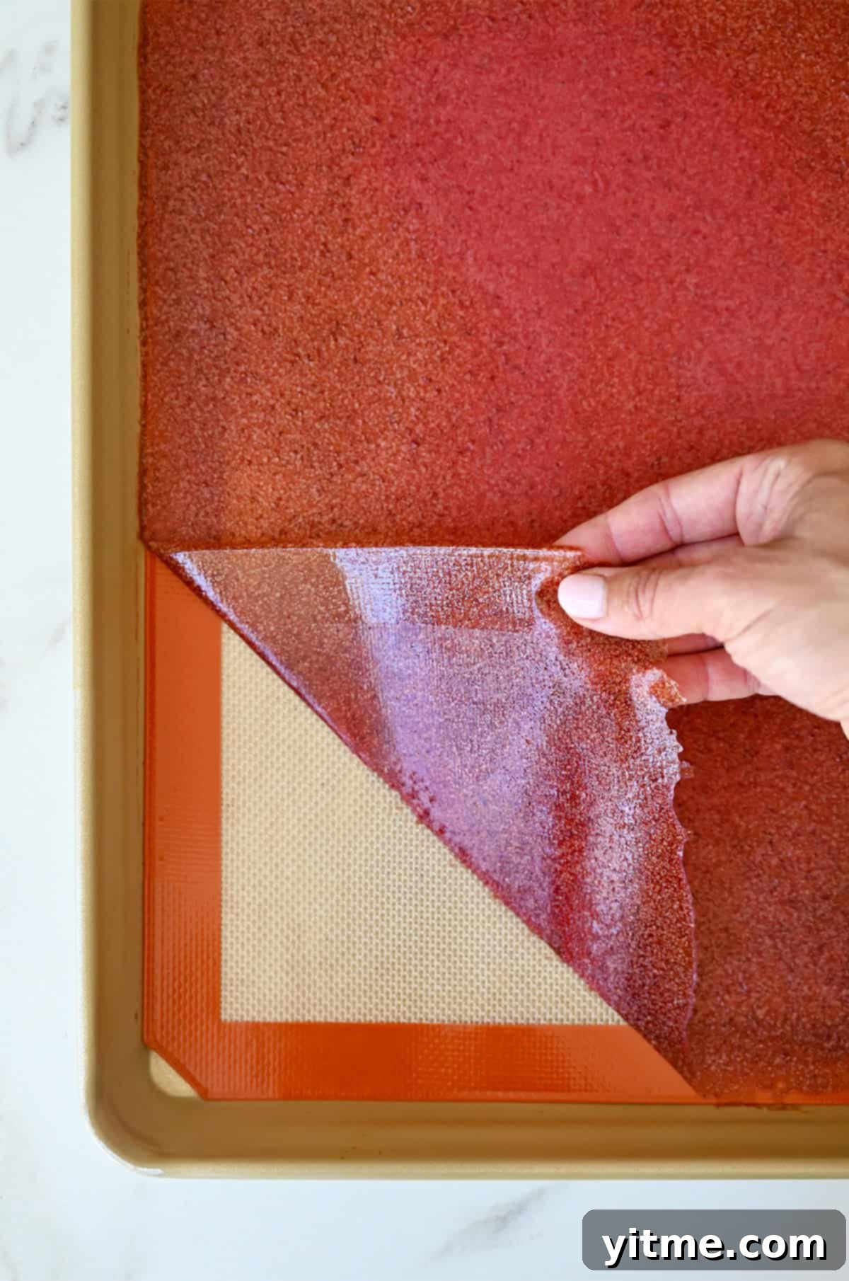 Strawberry fruit leather being peeled off a silicone baking mat.