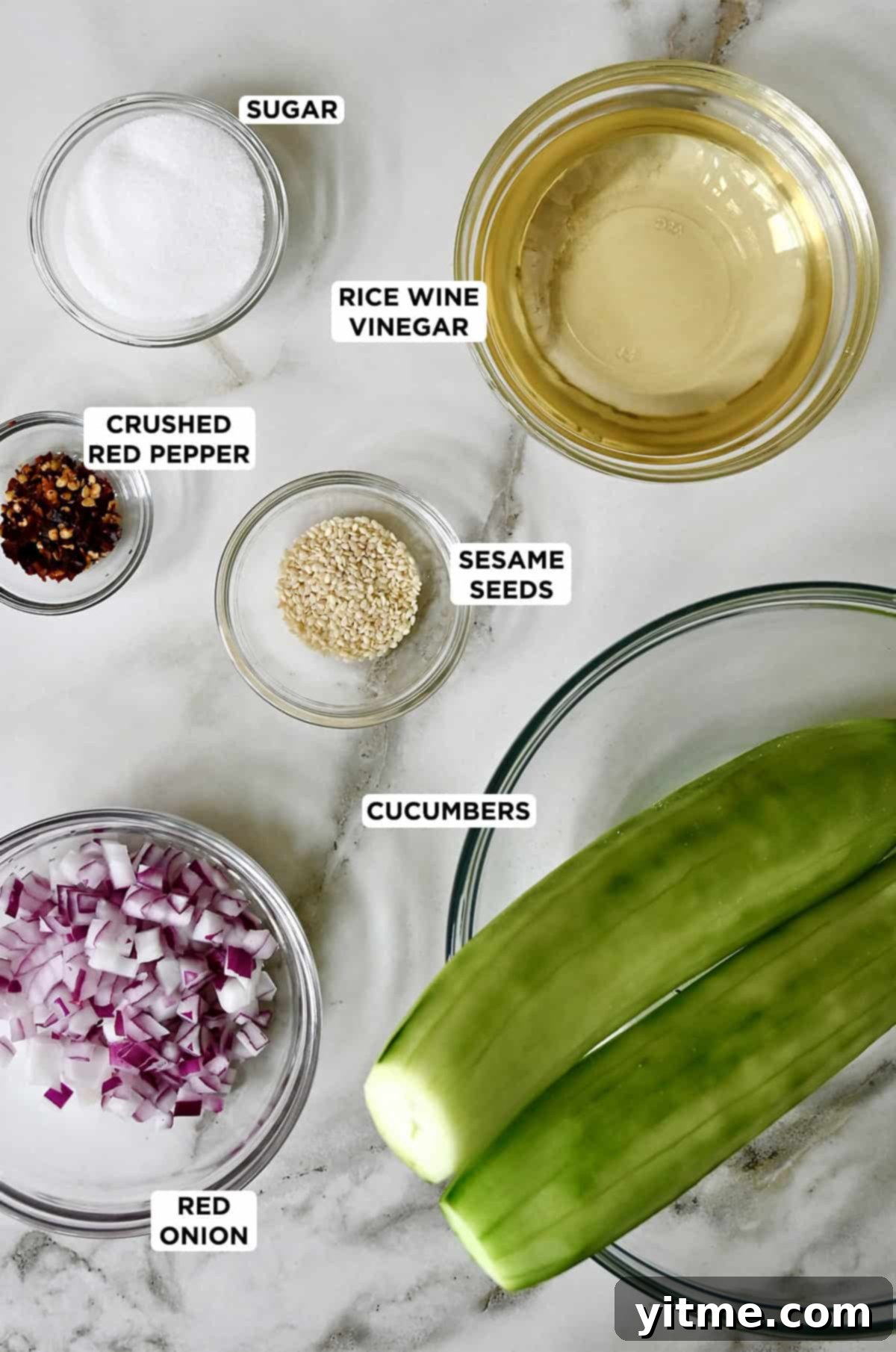 Ingredients for a simple cucumber salad: cucumbers, red onion, sesame seeds, red pepper flakes, sugar, and rice wine vinegar.