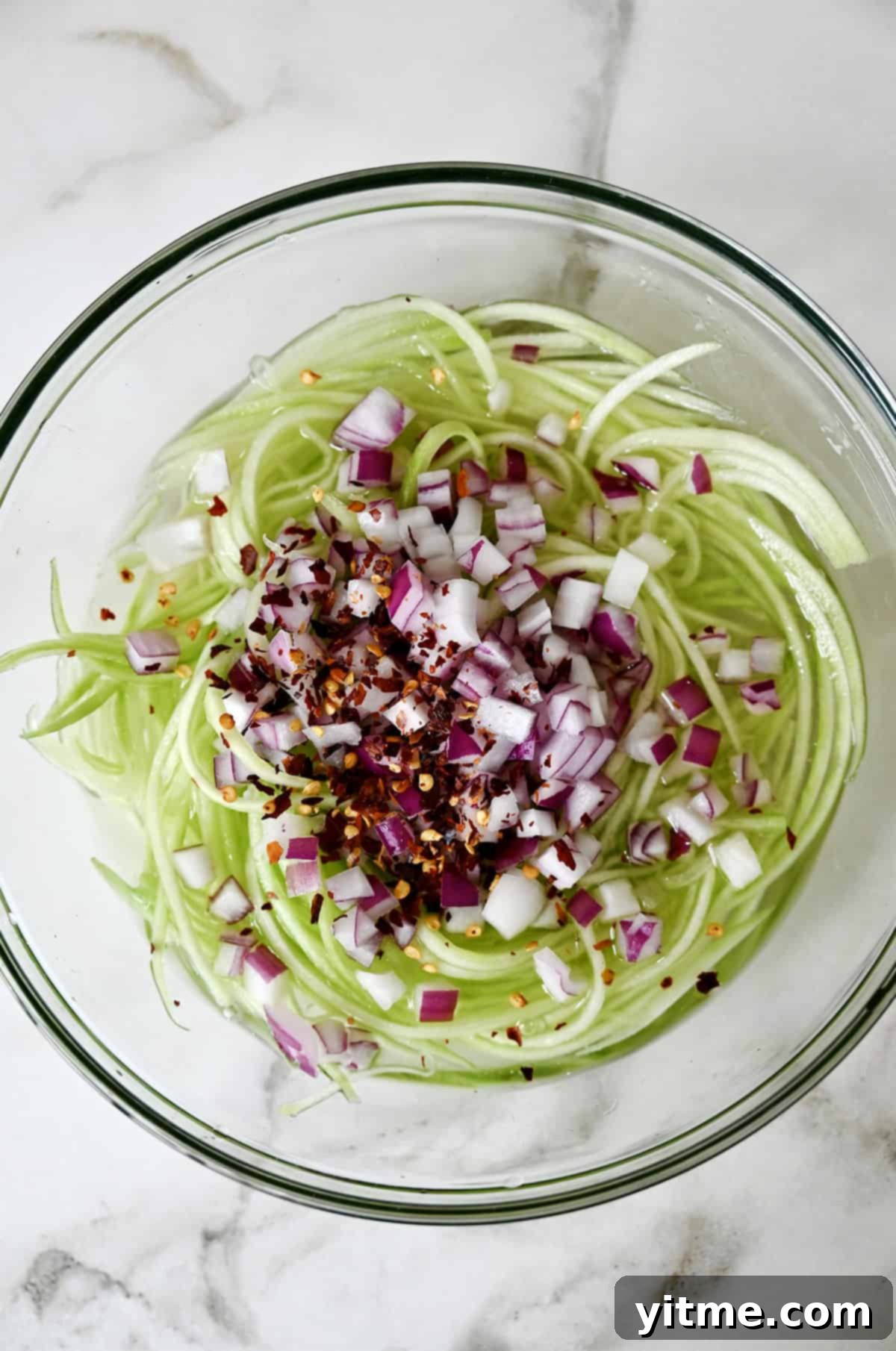 Crunchy Asian cucumber salad with a sweet and sour dressing, diced red onions, and chili flakes in a glass bowl.
