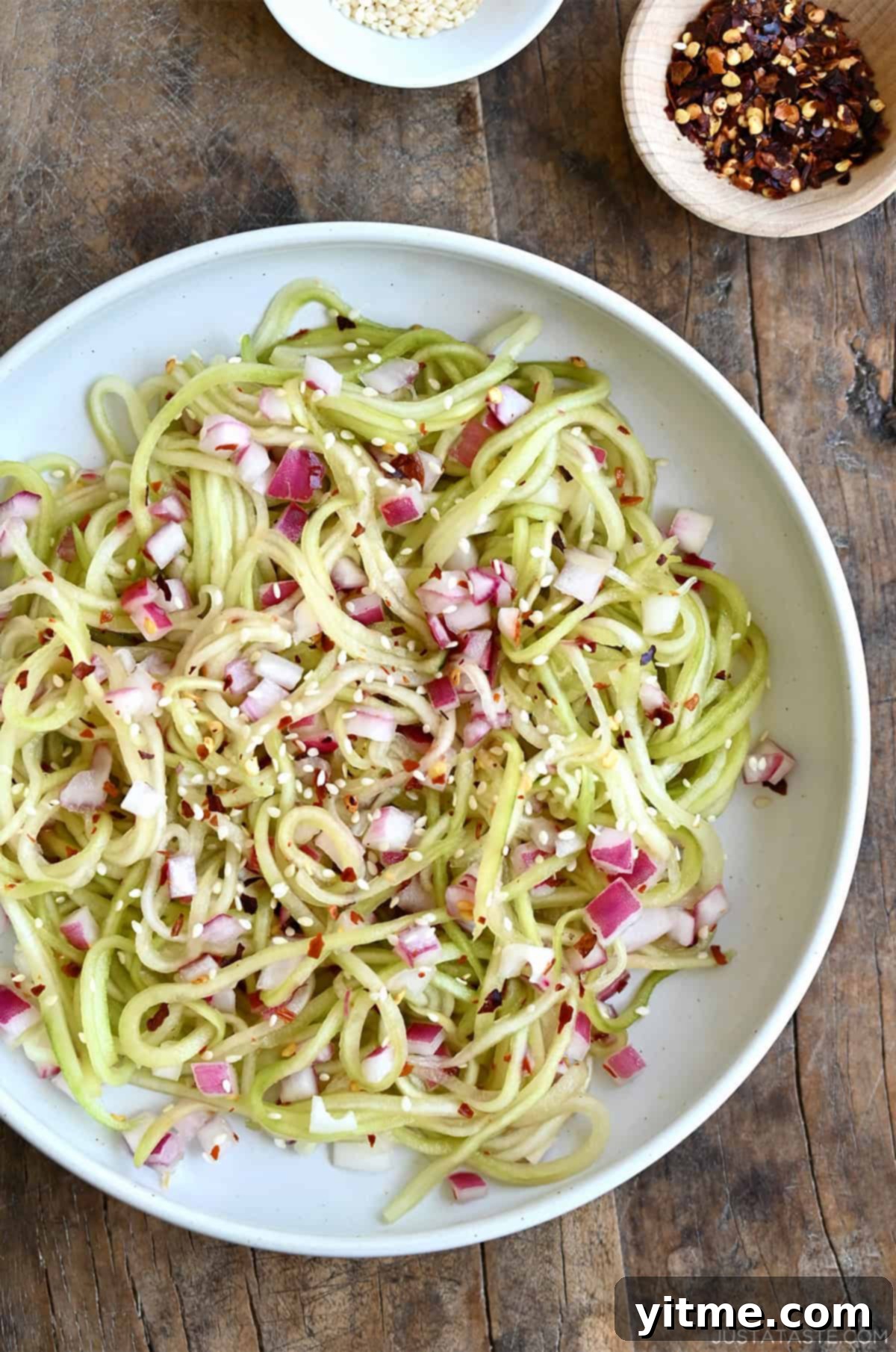 Asian cucumber noodles with diced red onion, red pepper flakes, and sesame seeds all tossed in a simple sweet and sour dressing.