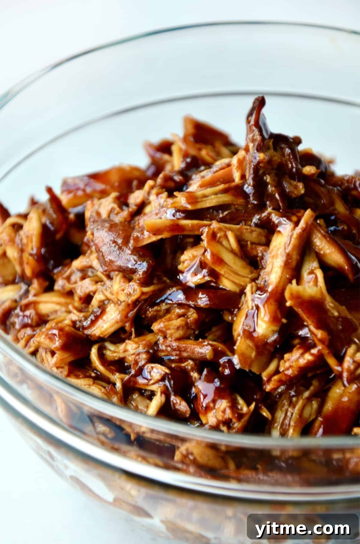 Pulled honey garlic chicken in a glass bowl.