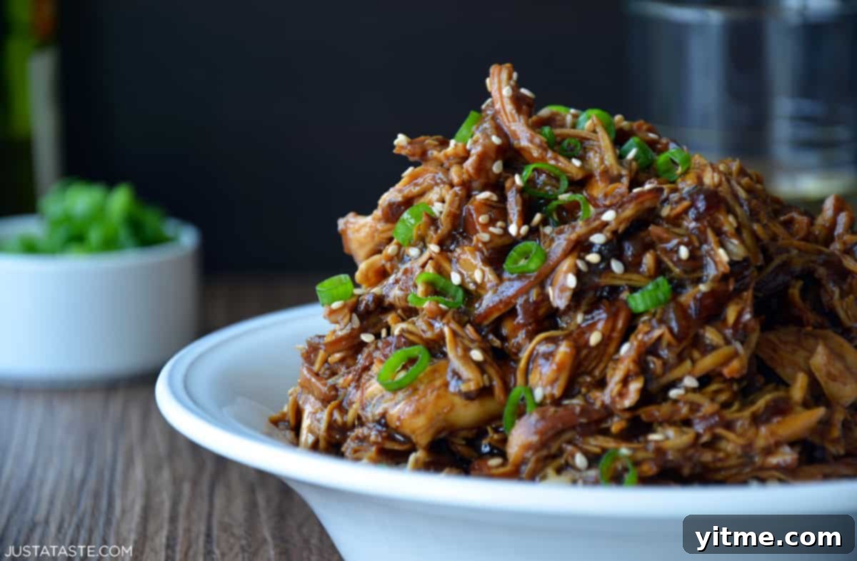 Shredded honey garlic chicken garnished with sesame seeds and sliced scallions over brown rice in a white bowl.