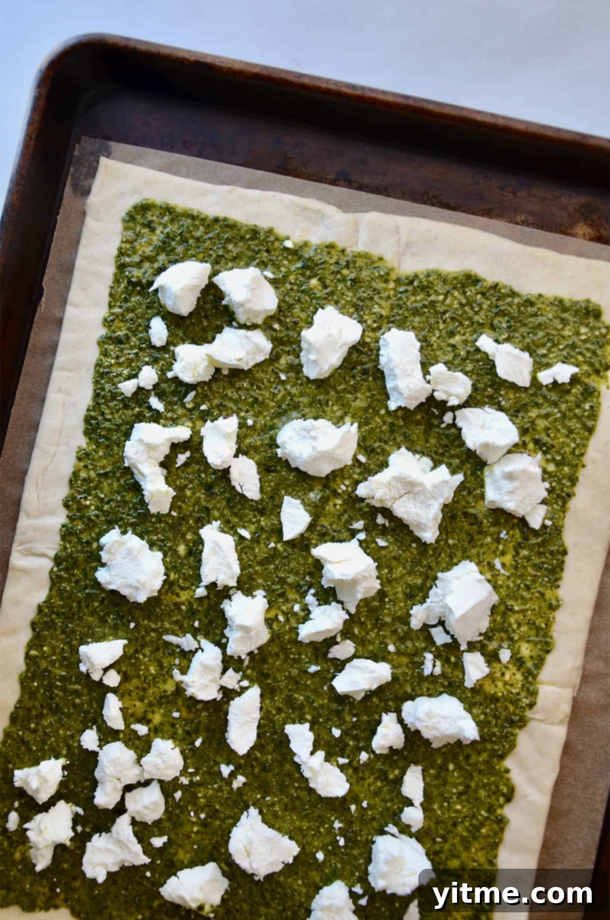 A rectangle of puff pastry topped with pesto and crumbled goat cheese.